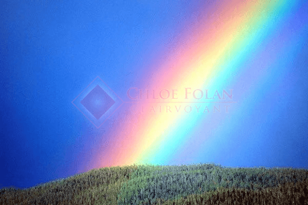 Rainbow landing on green hills with overlaid watermark for Chloe Folan Clairvoyent.
